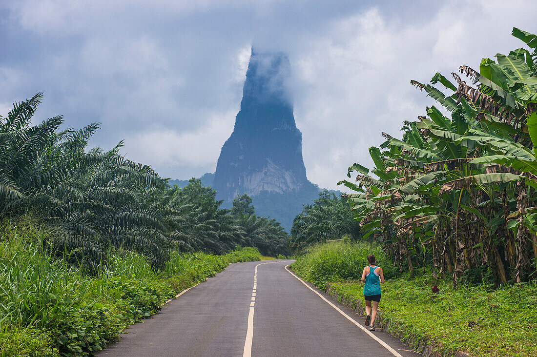 Runner on a road leading to the unusal monolith, Pico Cao Grande, east coast of Sao Tome, Sao Tome and Principe, Atlantic Ocean, Africa