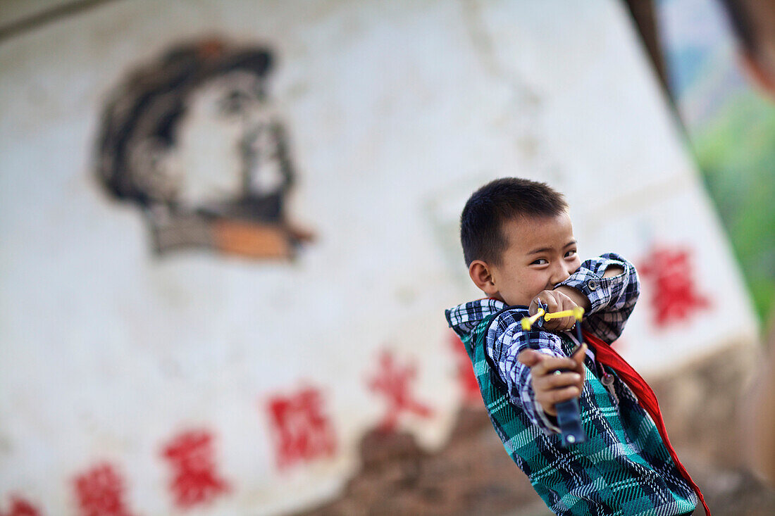 Boy with slingshot in front of Chairman Mao mural, Yunnan, China