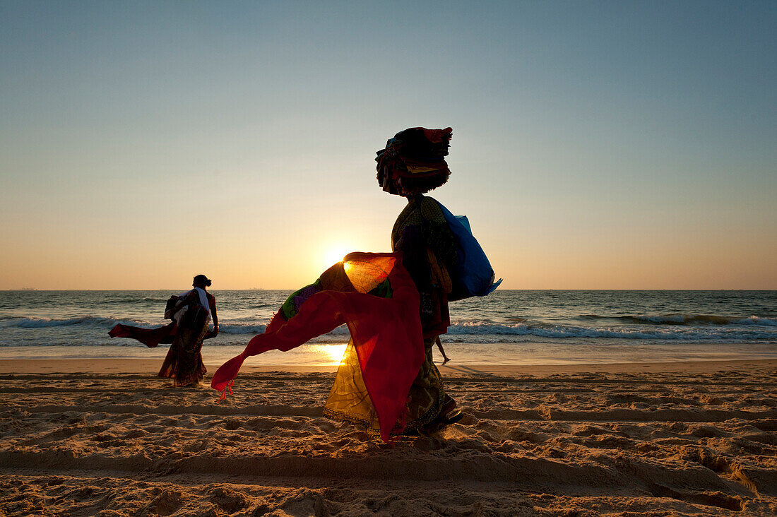 Silhouette of a woman selling Indian cloth on the beach at dusk, Candolim, Goa, India