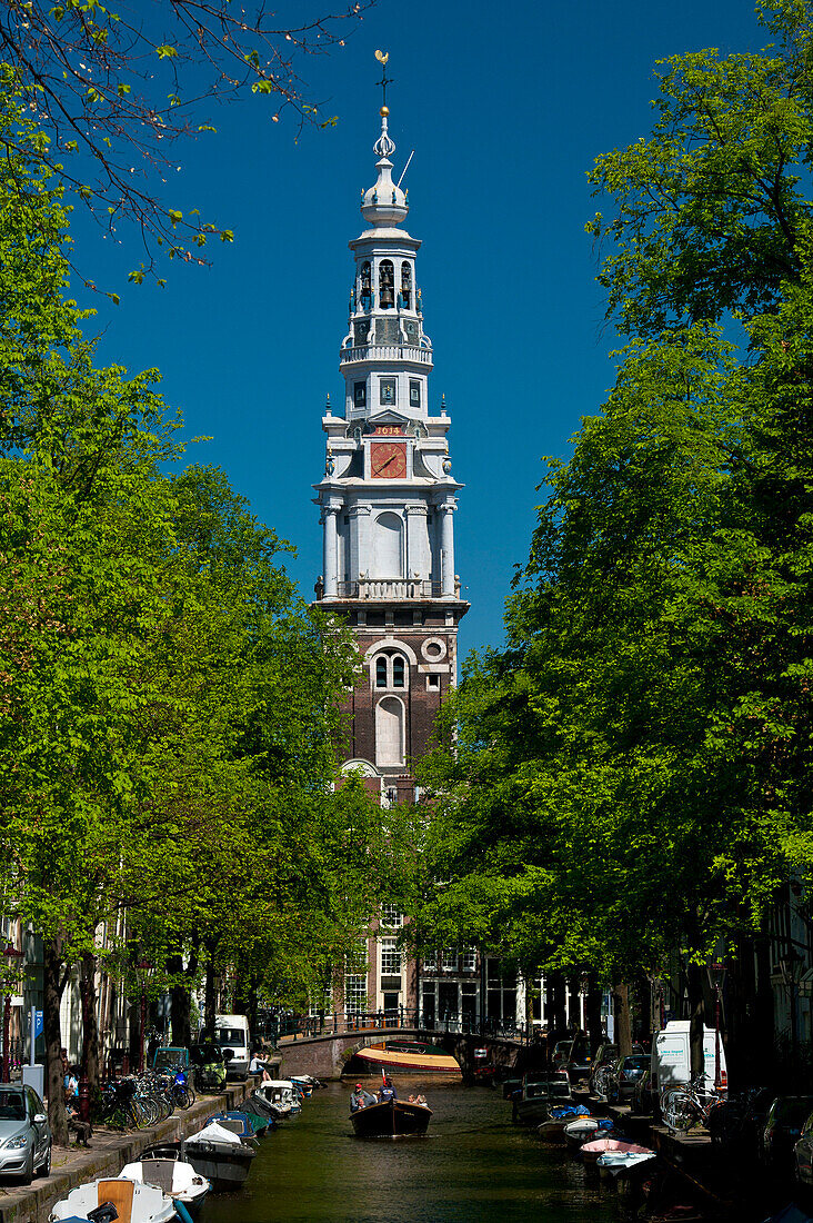 People in small boat going along small canal with spire of the Zuiderkerk church behind, Amsterdam, Holland