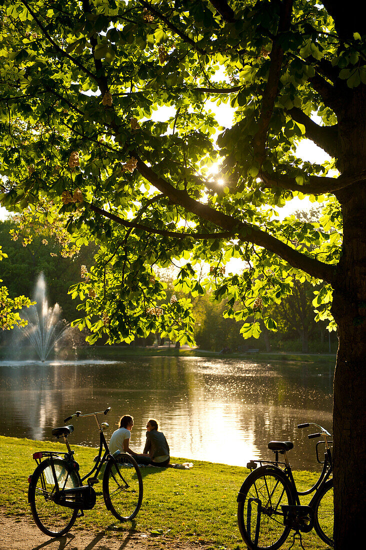Couple relaxing beside lake in the Vondelpark in the evening, Amsterdam, Holland