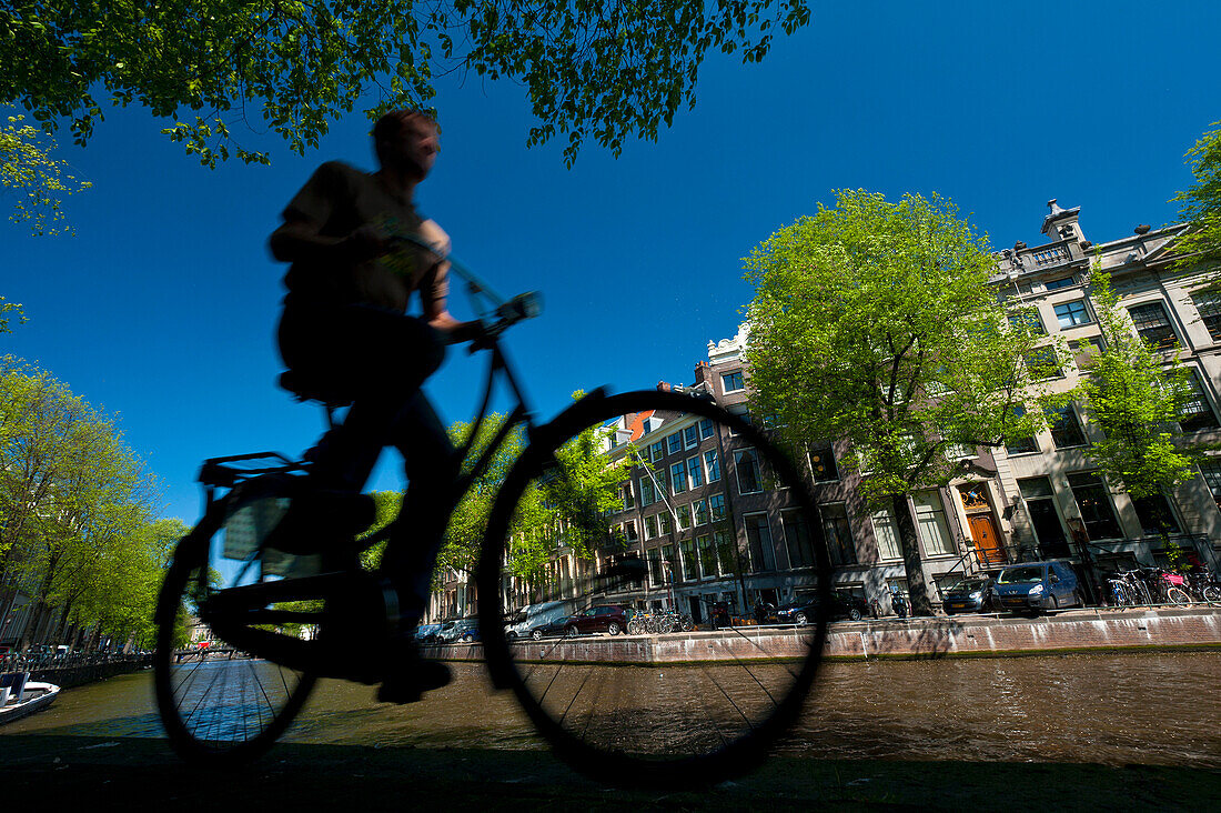 Silhouette of man cycling past canal, Amsterdam, Holland