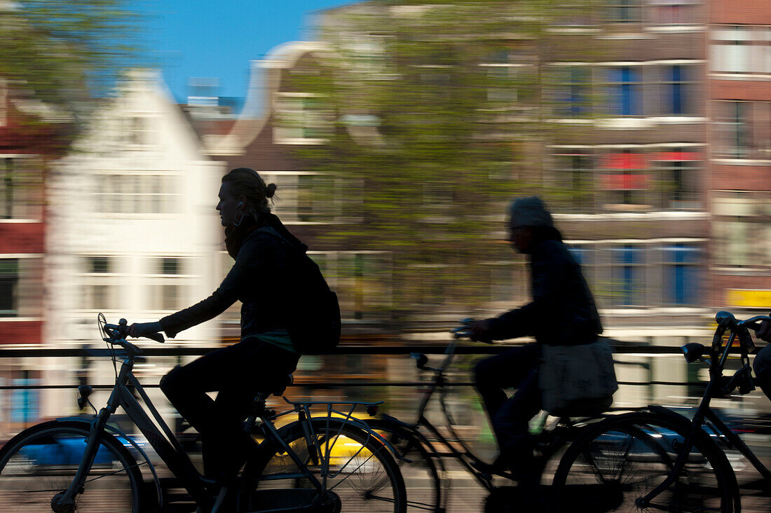 Silhouette of cyclists going past canal and gabled houses, Amsterdam, Holland