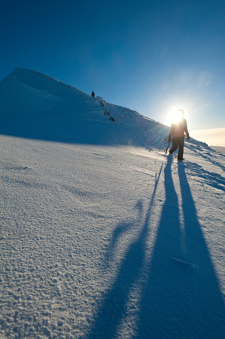 Walkers descending the snowy slopes of Sgorr Dhearg in winter near Glen Coe, Highlands, Scotland