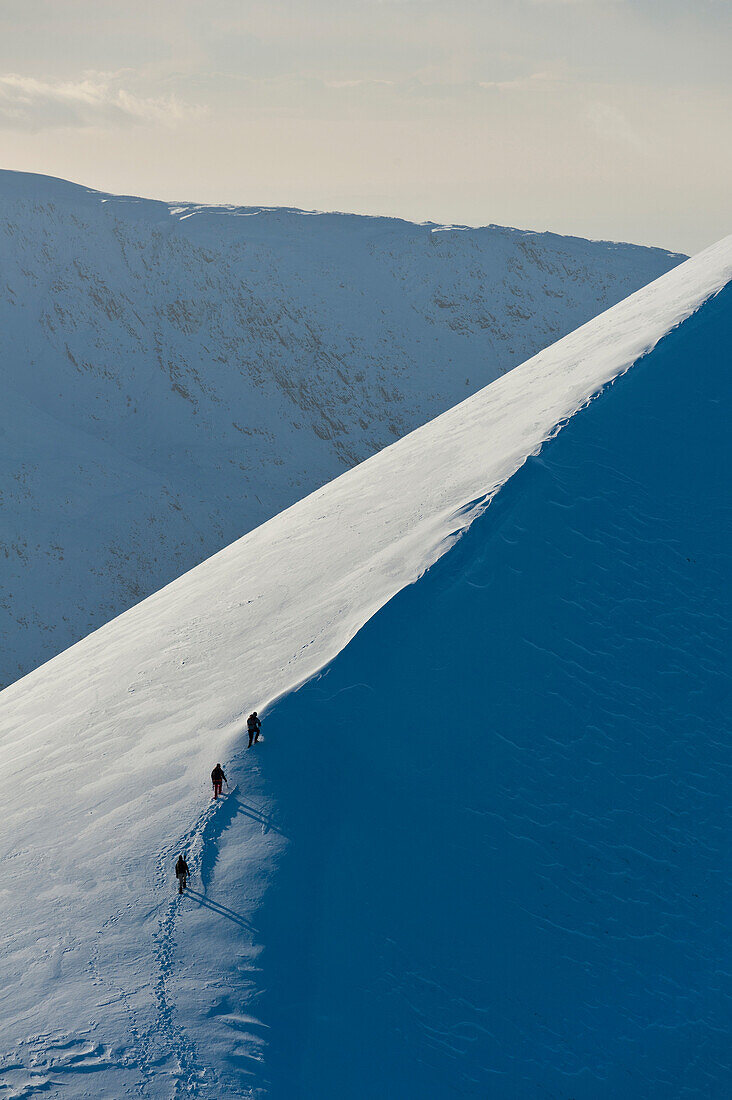 Walkers climbing snowy ridge of Sgorr Dhearg in winter near Glen Coe, Highlands, Scotland