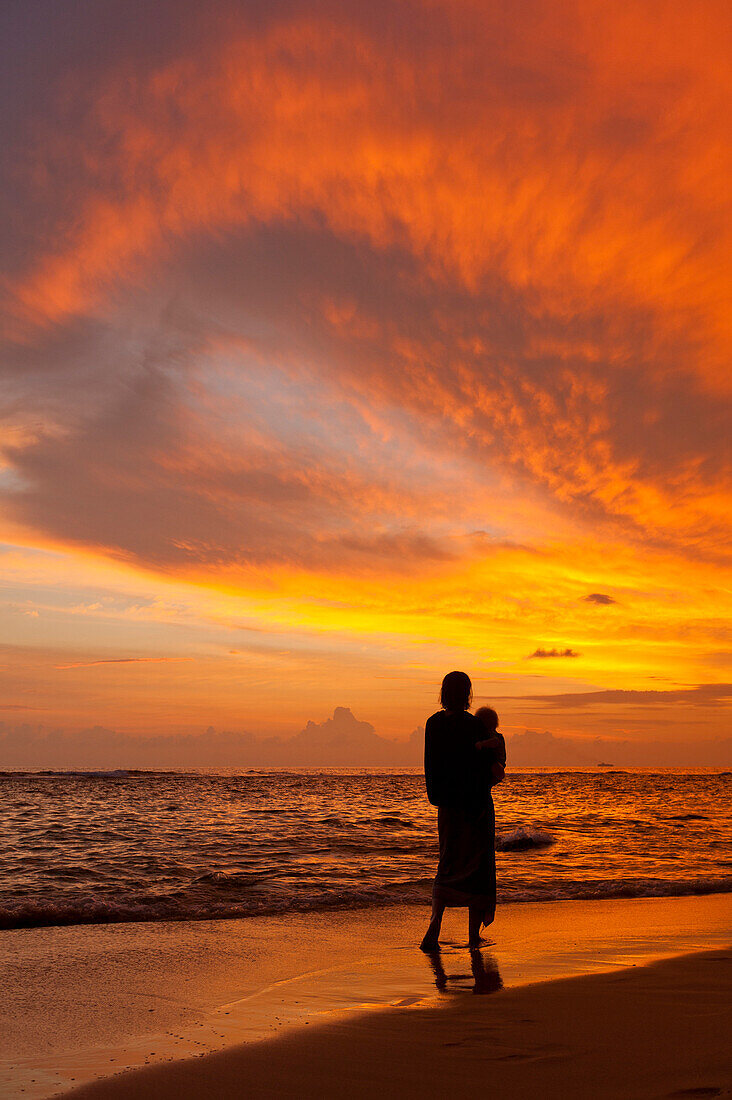 Mother and baby watching sunset on beach, near Unawatuna, Thalpe, Sri Lanka