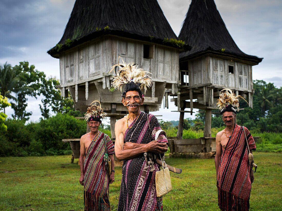 Elderly men in traditional attire standing in front of distinctive houses, Timor-Leste