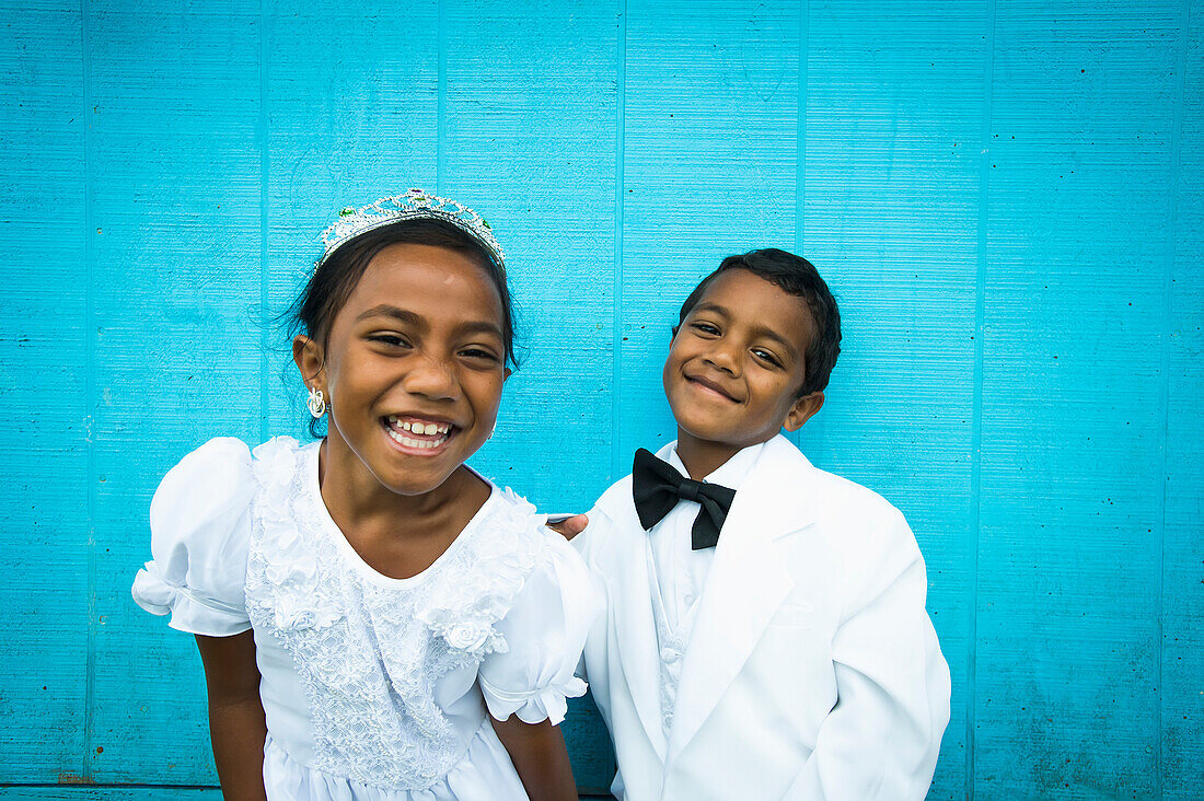 Children dressed in white formal wear against a blue wall, Hapai Island, Tonga