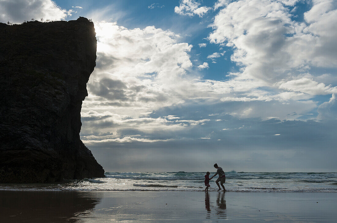 Mother and daughter dodging waves on beach at Bedruthan Steps, Cornwall, England