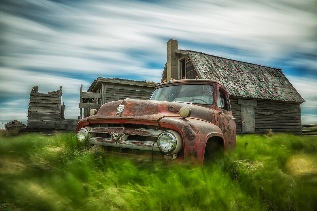 'Long exposure of clouds drifting by over an abandoned truck and house in a rural area; Saskatchewan, Canada'