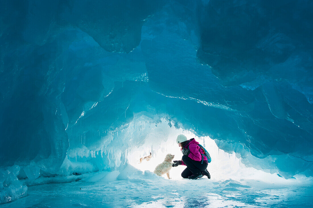 'Woman with her pet dog inside a natural ice cave on frozen Lake Superior in winter; Ontario, Canada'
