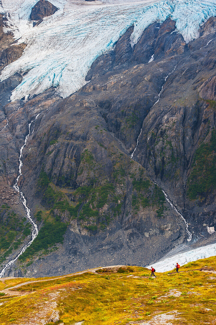 A man and woman hiking down the Harding Icefield Trail with Exit Glacier in the background, Kenai Fjords National Park, Kenai Penninsula, Southcentral Alaska