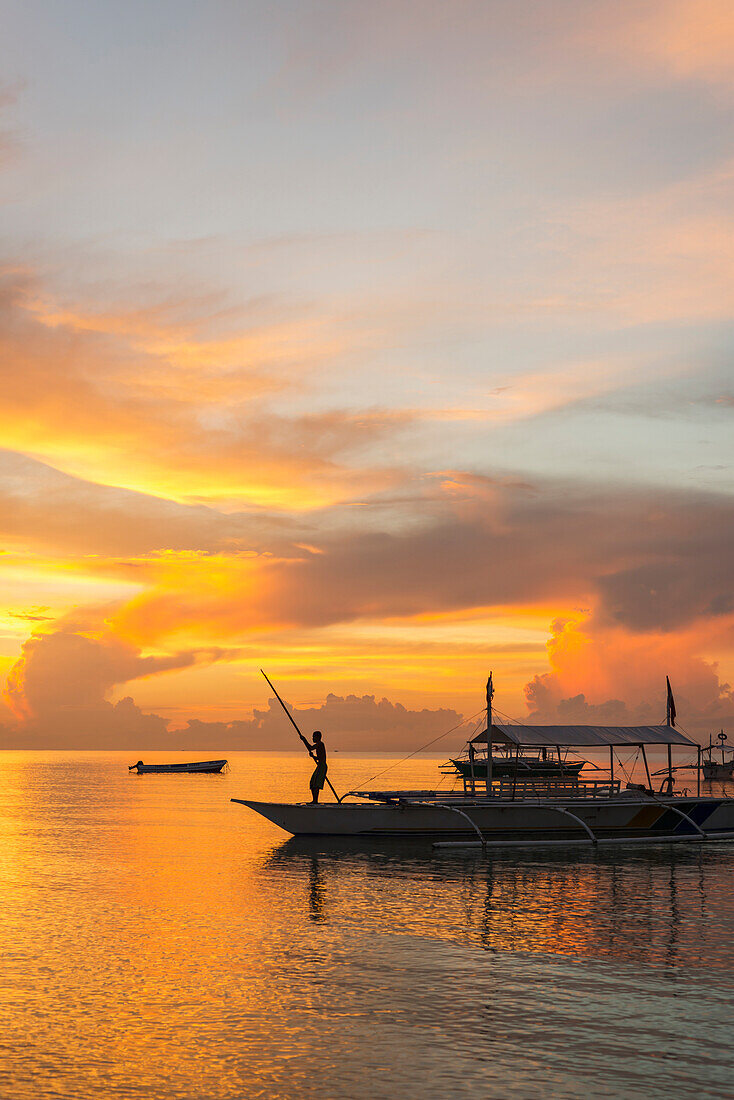 Beautiful sunrise in Alona Beach, a man moving his boat to reach the shore with a long stick, Panglao Island, Bohol, Philippines