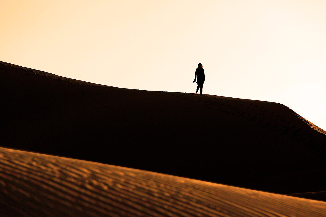 Morocco, Draa Valley, Tinfou, Tinfou dunes, Young woman walking on the dunes at sunrise