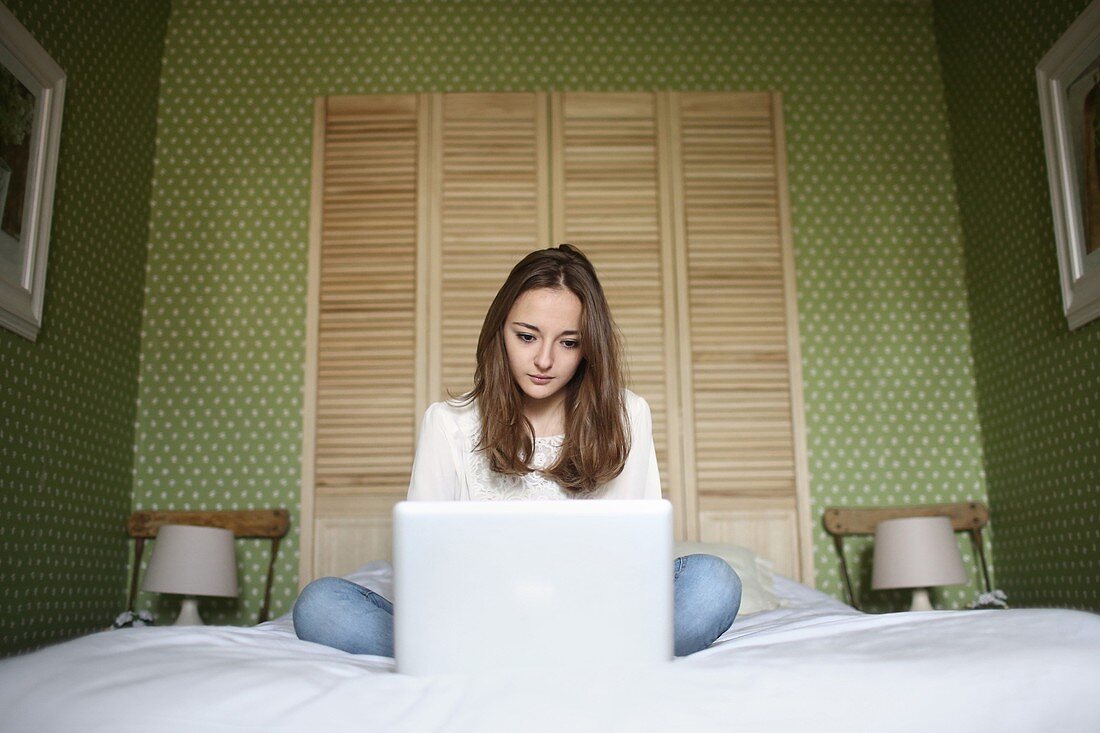 A teenage gril consulting her laptop on her bed