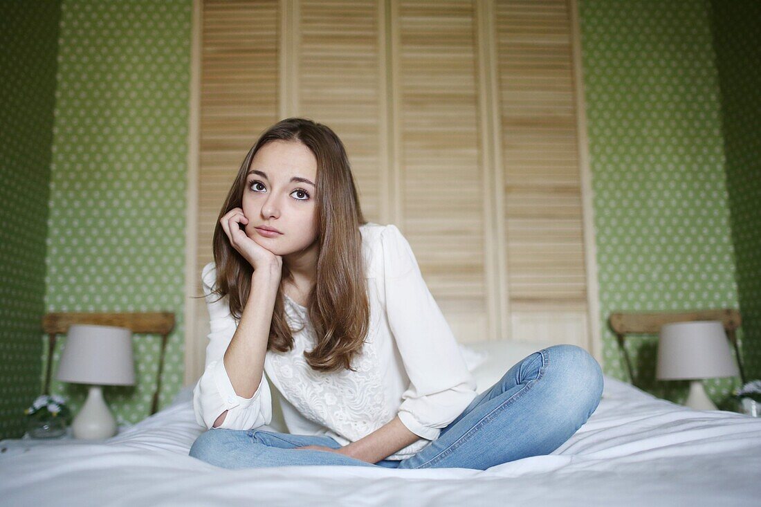 A teenage girl looks dreamy sitting on her bed