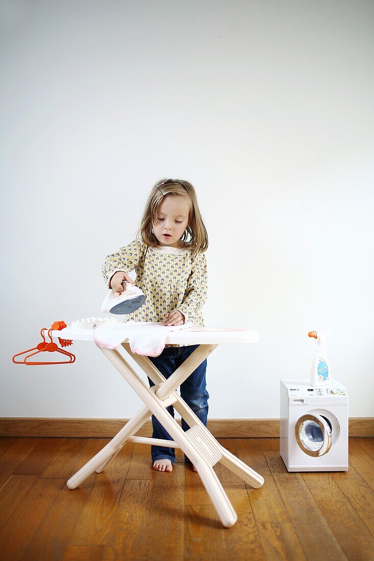 A 3 years old girl playing with an iron and ironing board for child