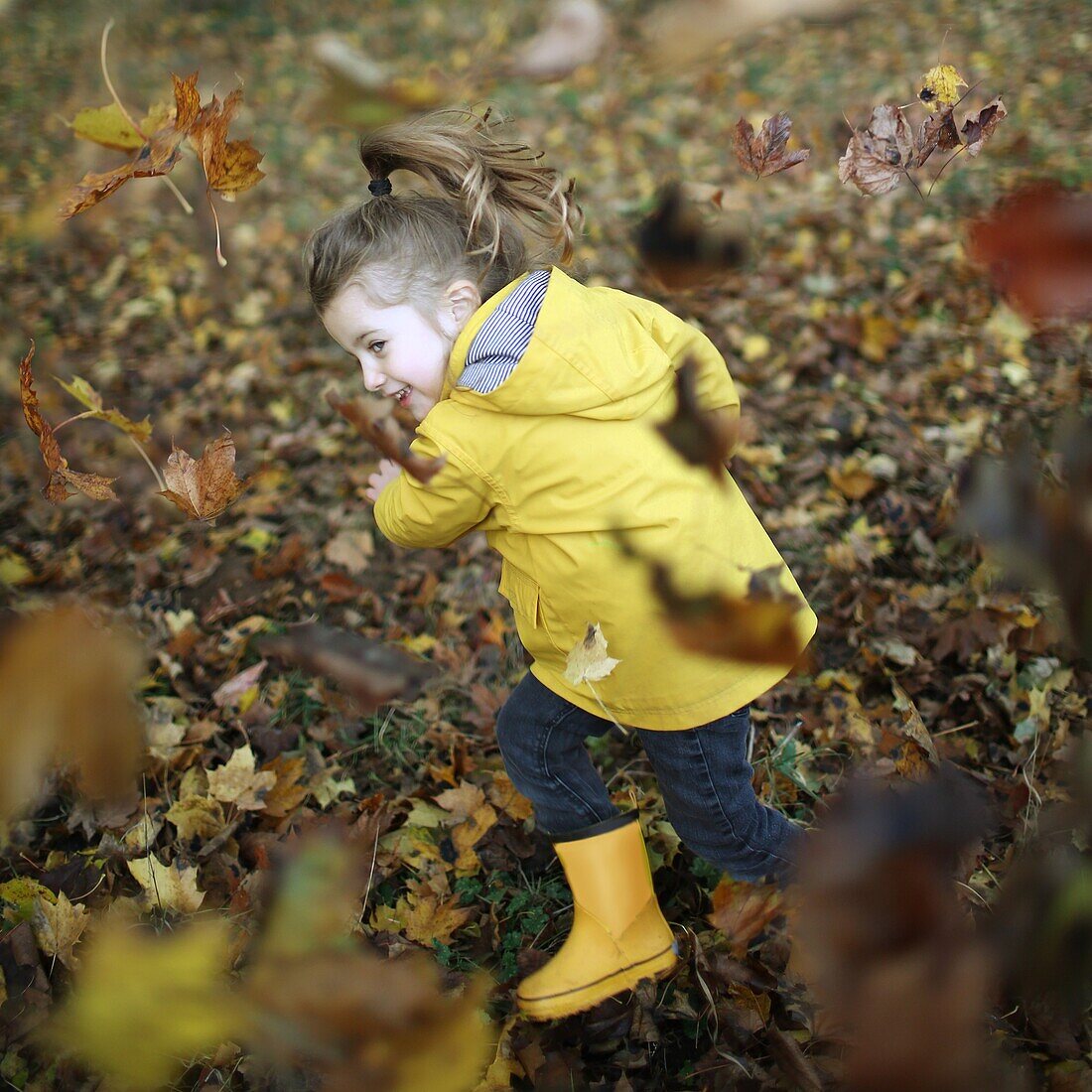A little girl playing with dead leaves