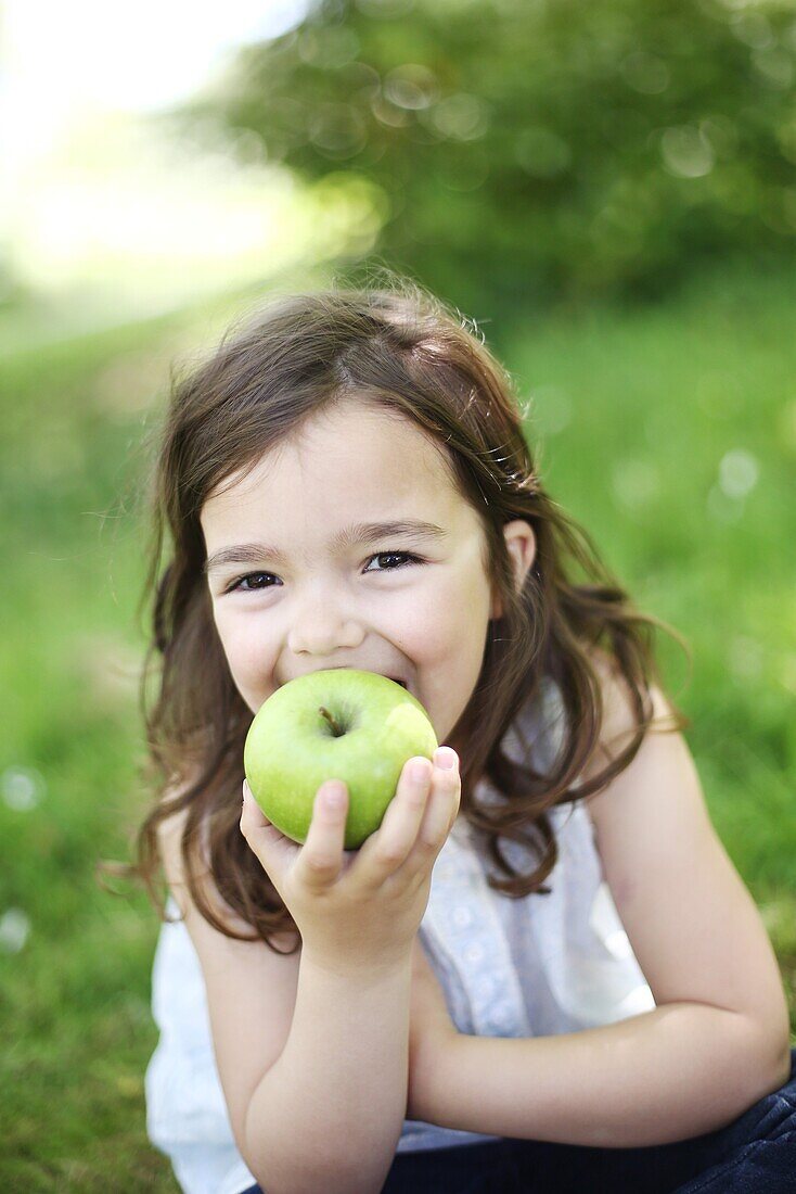 A 5 years old girl eating an apple in the countryside