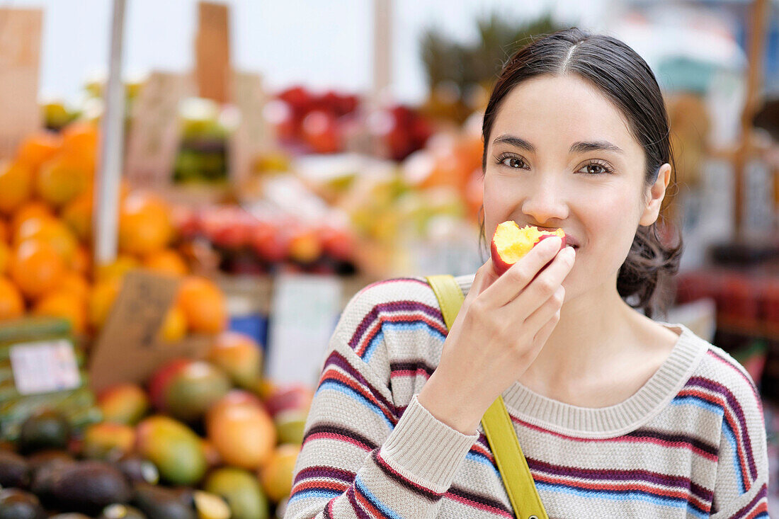 Hispanic woman eating fruit at farmers market