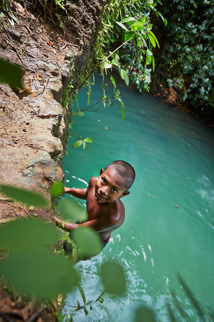 Boy jumping from rocks into the water, forest is part of the Ram Krishna Pur Dam, reservoir inland near Butler Bay Beach, northern Can Hat Bay, Little Andaman, Andaman Islands, Union Territory, India