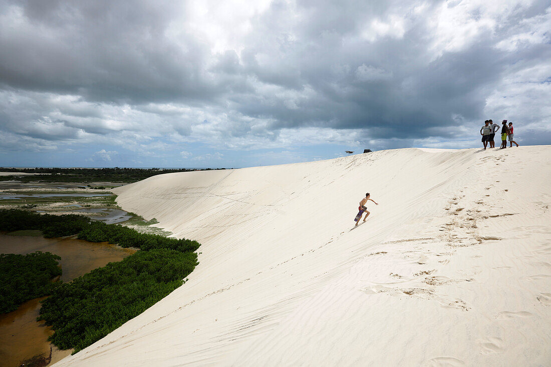 Auf Sandduenen von Tatatjuba, Jungen aus dem Dorf vermieten selbstgebaute Sandboards an Besucher, Lagunen sind von Regenwasser gefuellt, Tatatjuba, westlich Jericoacoara, Ceara, Brasilien