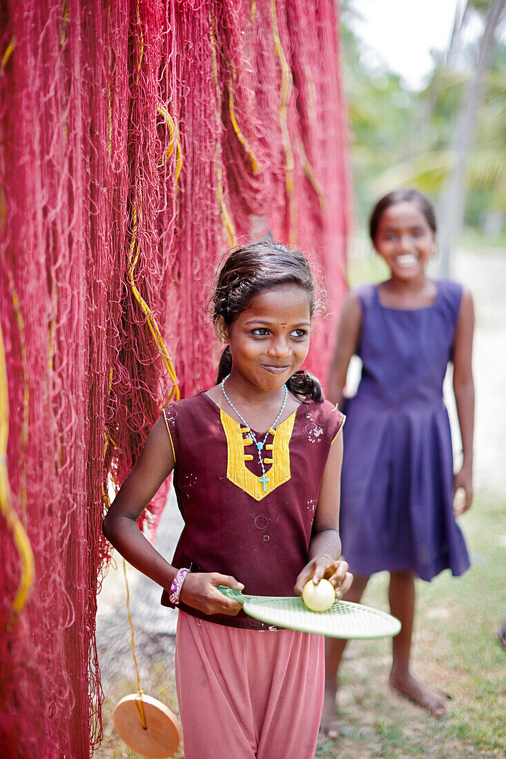Christian girl in front of drying fishing nets which are hanging between palm trees, fishing huts in Mararikulam, south of Kochi, Kerala, India