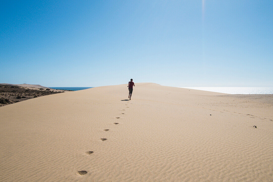 Caucasian teenage boy running on sand dune