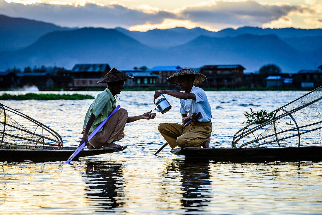 Asian fishermen sharing tea in canoes on river