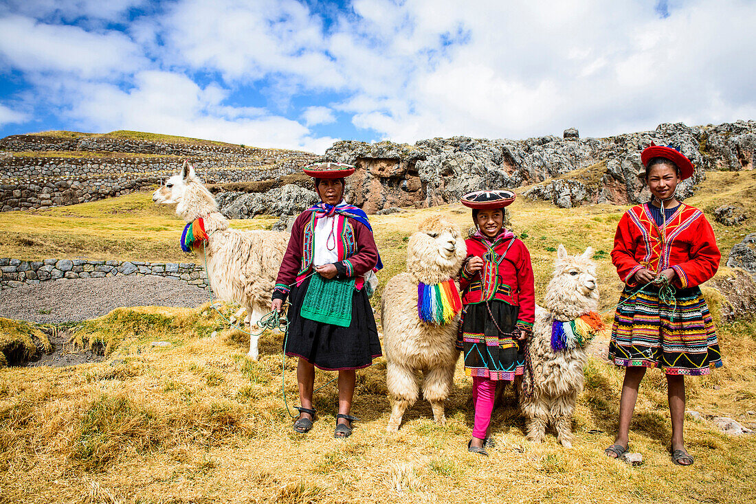 Hispanic mother and children standing with llamas in rural landscape