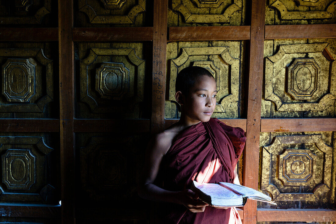 Asian monk-in-training holding book in temple