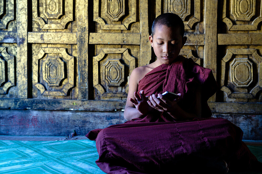 Asian monk-in-training using cell phone in temple