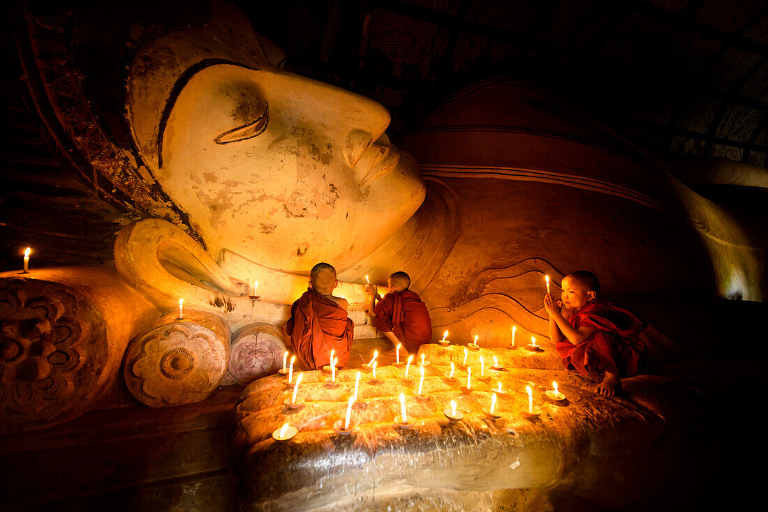 Asian monks-in-training lighting candles at Buddha statue