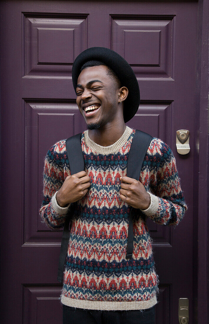 Laughing Black man wearing backpack near purple door