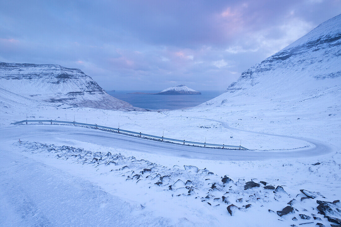 Snow covered road winding down between mountains near Nordradalur on the Island of Streymoy, Faroe Islands, Denmark, Europe