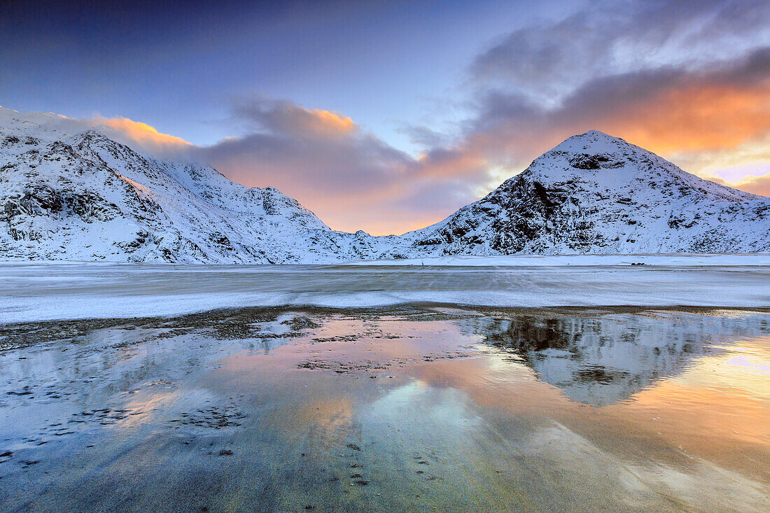 Sunrise on Uttakleiv beach surrounded by snow covered mountains reflected in the cold sea, Lofoten Islands, Arctic, Norway, Scandinavia, Europe