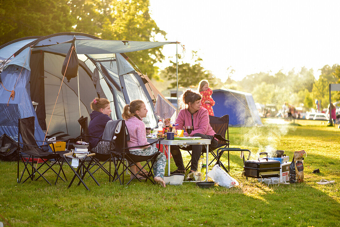 Family camping, mother and two daughters with barbecue in front of tent, camping ground, Vaestervik, Smaland, Sweden