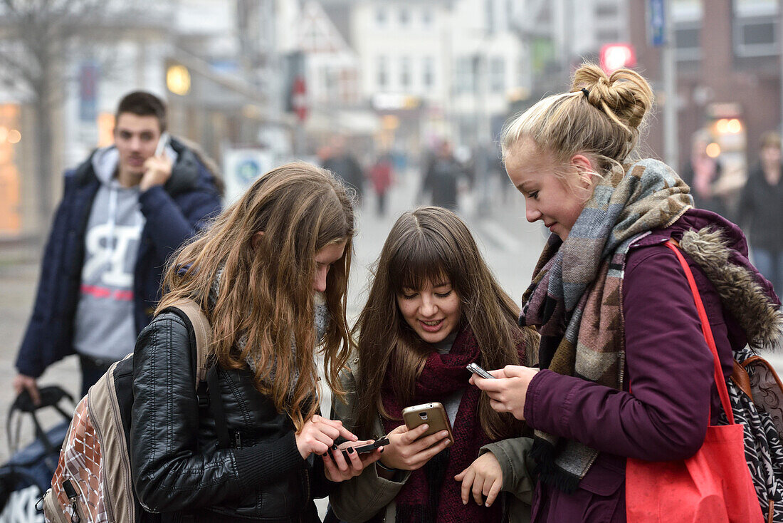 3 girls chatting on their smartphones in the city centre, Hamburg, Germany, Europe