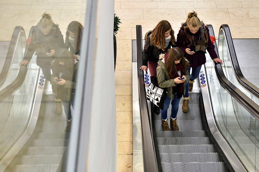 3 Girls chatting with smartphones in a shopping mall on the escalator, Hamburg, Germany, Europe