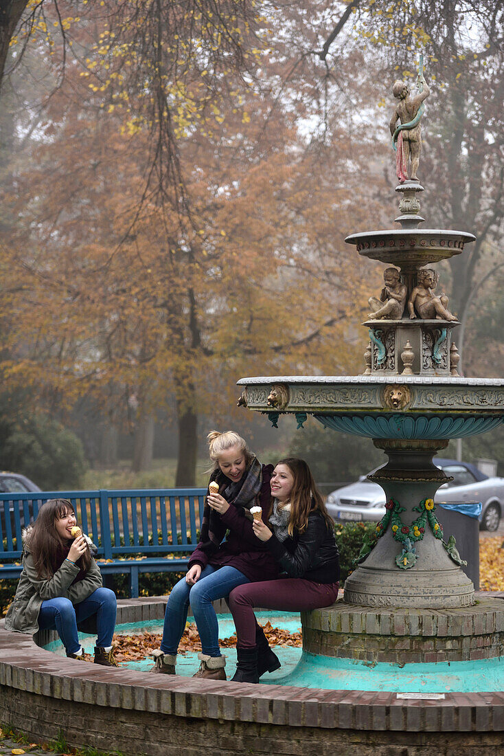 3 girls eating ice cream at the fountain in autumn, Hamburg, Germany, Europe