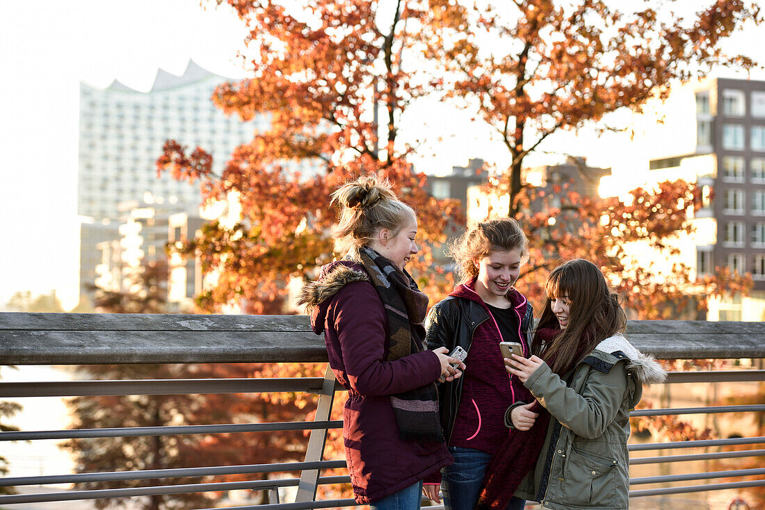 3 Mädchen mit Smartphones vor Elbphilharmonie, Hafencity, Hamburg, Deutschland, Europa