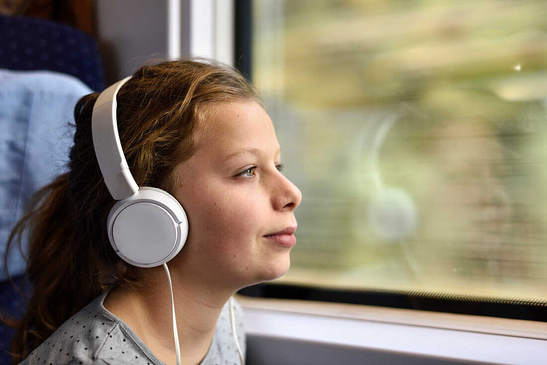 Girl listening to music with headphones in train, Germany, Europe