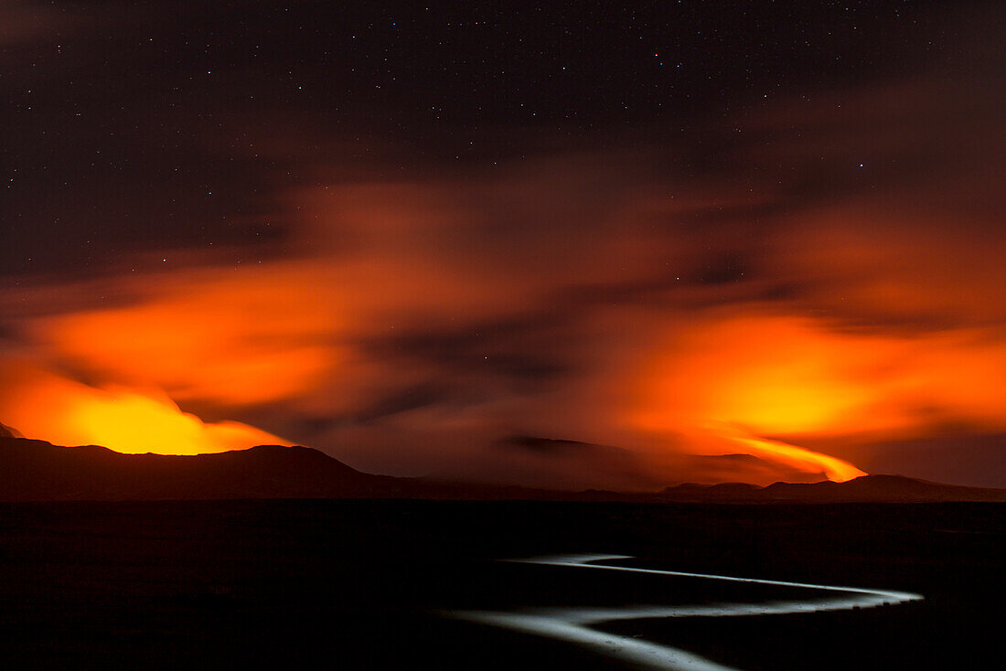 Views of the volcanoes Marum and Benbow in far distance at night. Lava shines at the gases and the night sky in red color. A flashlight markes a way into the black ashes, Vanuatu, Ambrym Island, South Pacific