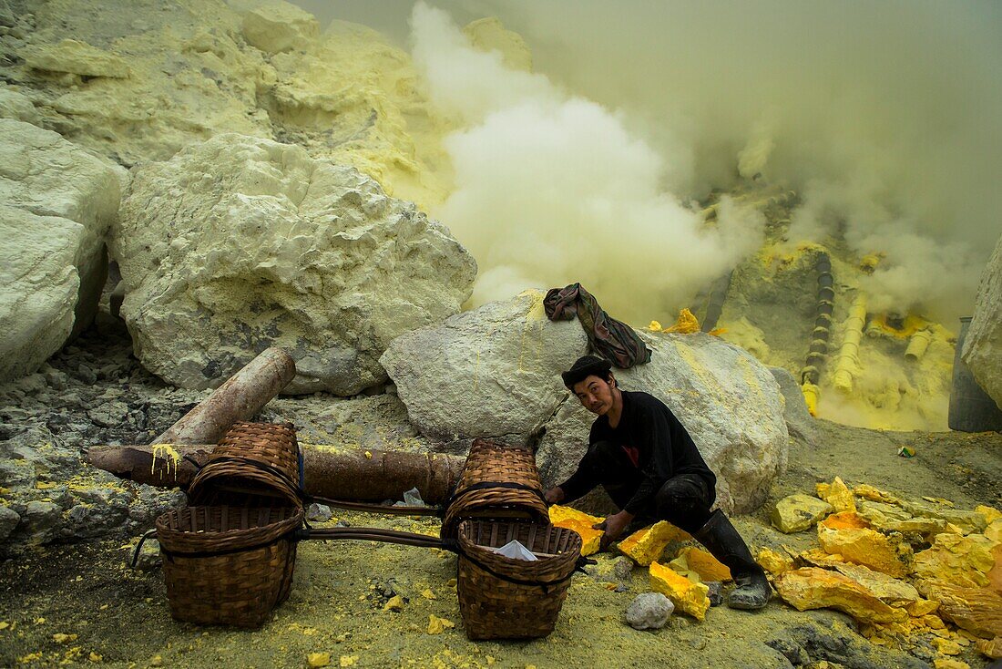Minenarbeiter steht im giftigen Schwefelgas der Teufelsmine im inneren des aktiven Vulkans Ijen auf Java und belädt Körbe mit erstarrten Schwefel, Ost-Java, Vulkan Ijen, Indonesien