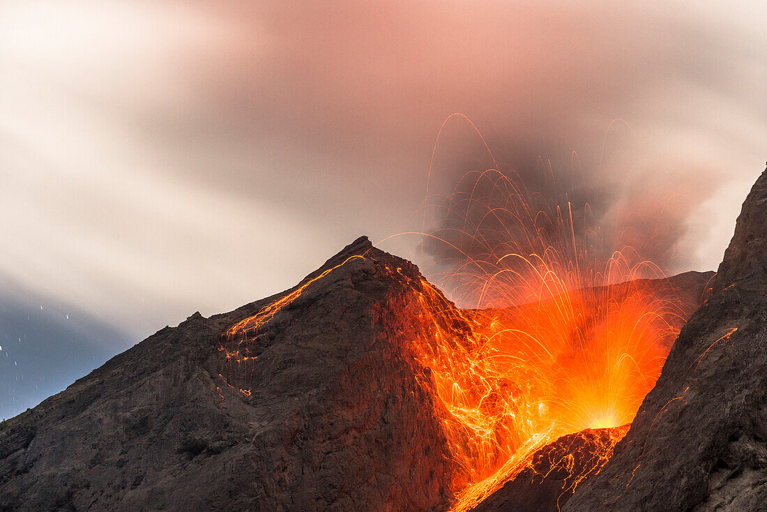 Große Eruption mit Lavaauswurf an der offenen Flanke des Vulkans Batu Tara in der Flores Sea bei Nacht mit Sternenhimmel und Vulkan-Gasen, Insel Komba, Flores Sea, Indonesien