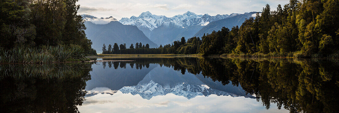 Mountains and forest reflecting in still lake, Mt Cook Village, South Westland, New Zealand