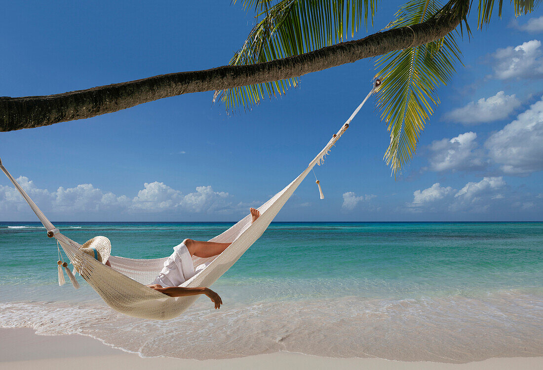 Caucasian woman laying in hammock under palm tree on tropical beach