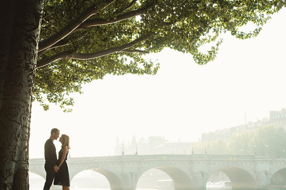 Caucasian couple kissing near bridge, Paris, Ile-de-France, France