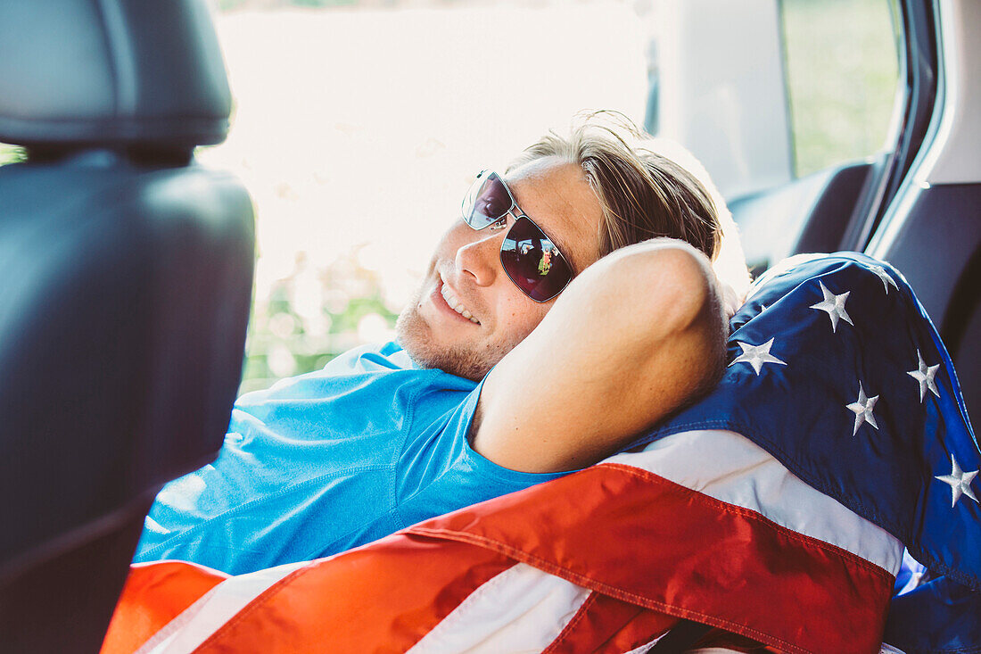Caucasian man laying on American flag in car