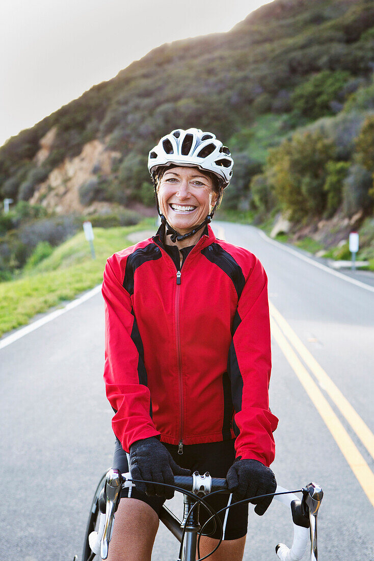 Caucasian woman with bicycle smiling on remote mountain road